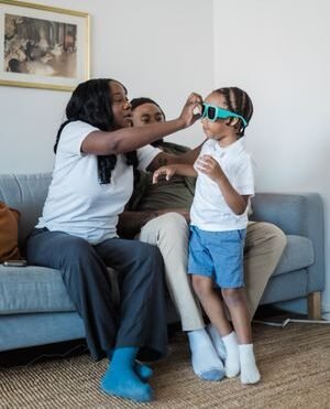 A joyful family moment with parents and child playing on the couch indoors, embracing happiness and togetherness.